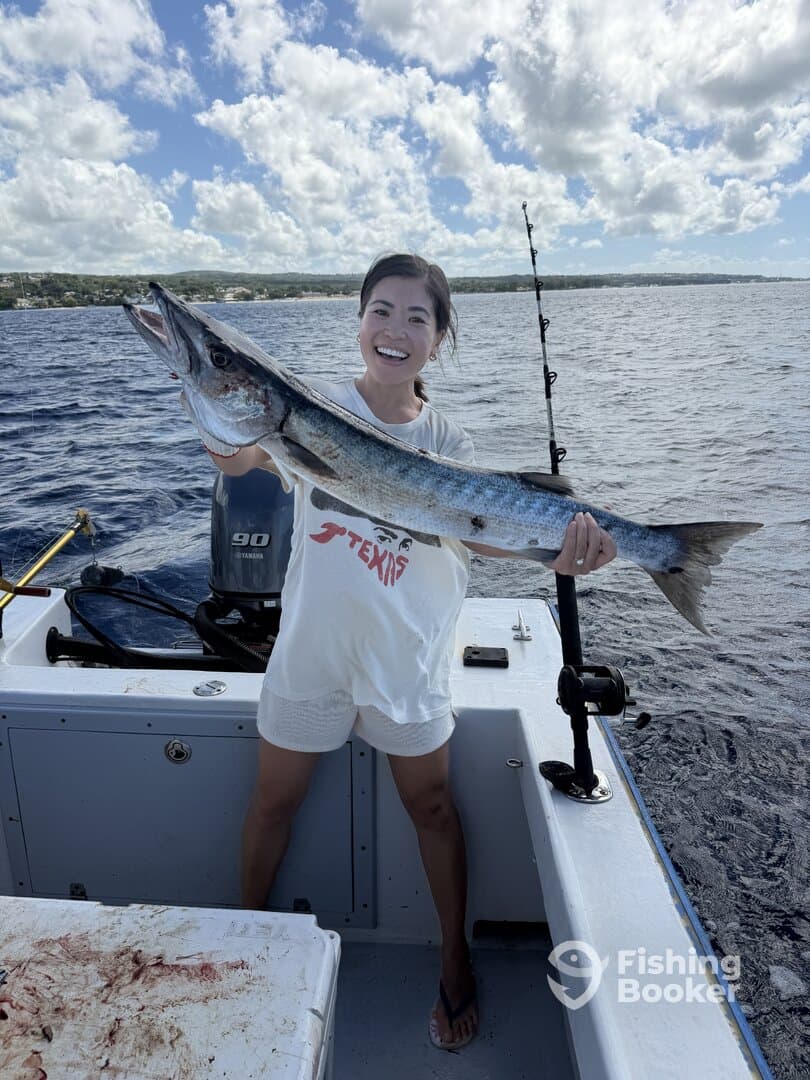 A smiling angler proudly displays a large Barracuda while fishing on a boat in clear blue waters.
