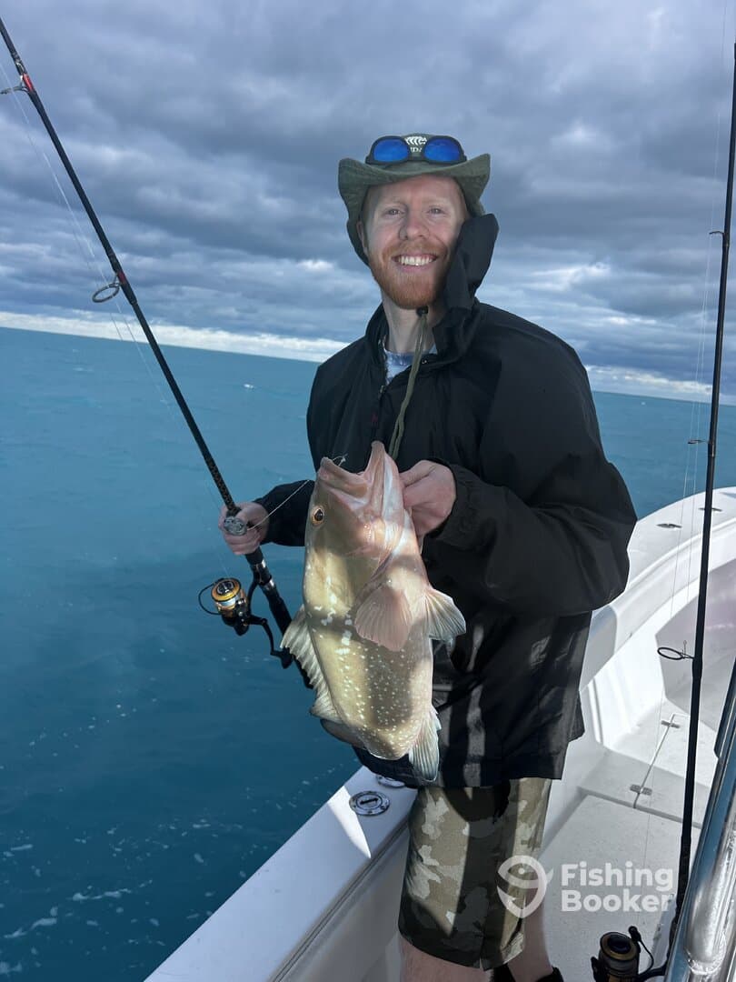 Angler proudly displaying a large Grouper while fishing on a boat in clear blue waters.
