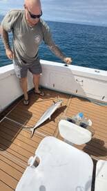 An angler is actively reeling in a Barracuda on the deck of a fishing boat, showcasing the excitement of sport fishing.