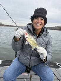 A smiling angler proudly displaying a striped bass while fishing on a calm lake, showcasing a successful day on the water.