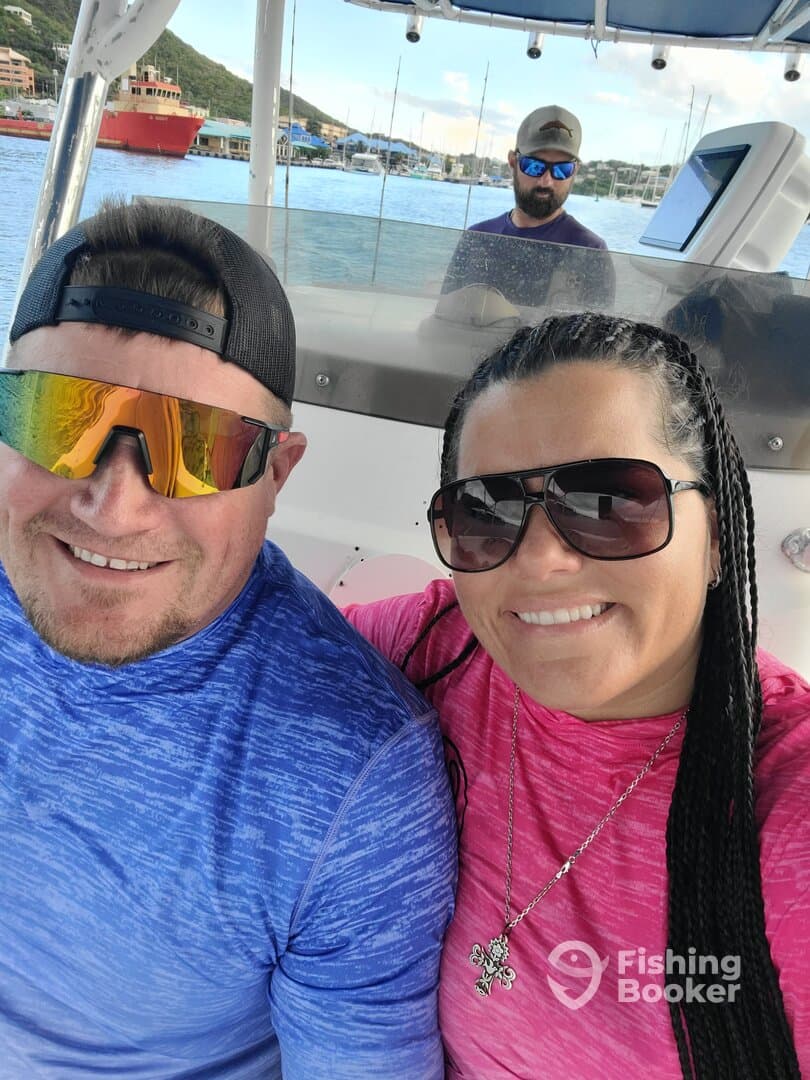 A couple enjoying a day on the boat, smiling for a selfie while the captain navigates in a scenic harbor.