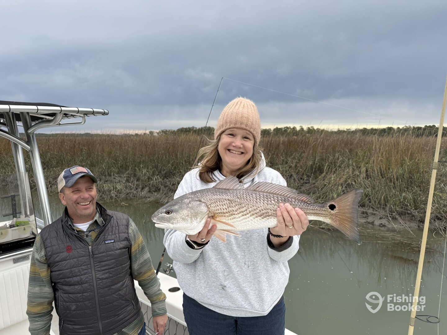 A happy angler proudly displaying a large Redfish while fishing in a scenic marsh environment.