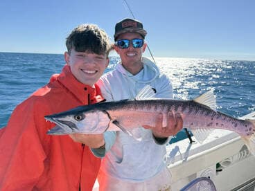 Two anglers proudly displaying a large Barracuda while fishing offshore, showcasing a successful day on the water.