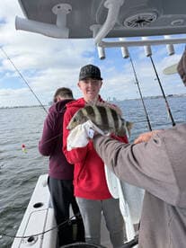 A young angler proudly displaying a striped fish while fishing on a boat, with fellow anglers in the background.