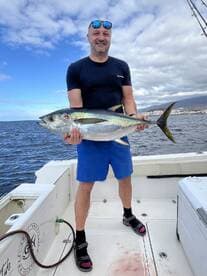 Angler proudly displaying a large Yellowfin Tuna aboard a fishing boat, showcasing a successful deep-sea fishing trip.