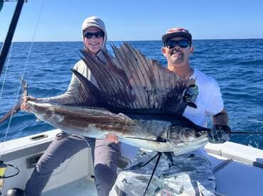 Two anglers proudly displaying a large Sailfish while out on the open ocean, showcasing their successful catch during a deep-sea fishing trip.