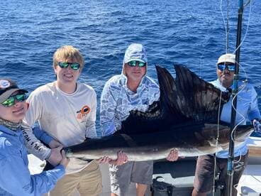 A group of anglers proudly displaying a large Sailfish while out on the open ocean, showcasing a successful fishing trip.