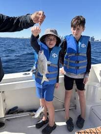 Two young anglers proudly displaying their catch of multiple fish while enjoying a day on the water.