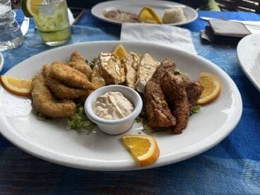 A plate of assorted fried and grilled fish dishes garnished with orange slices, served in a casual dining setting.