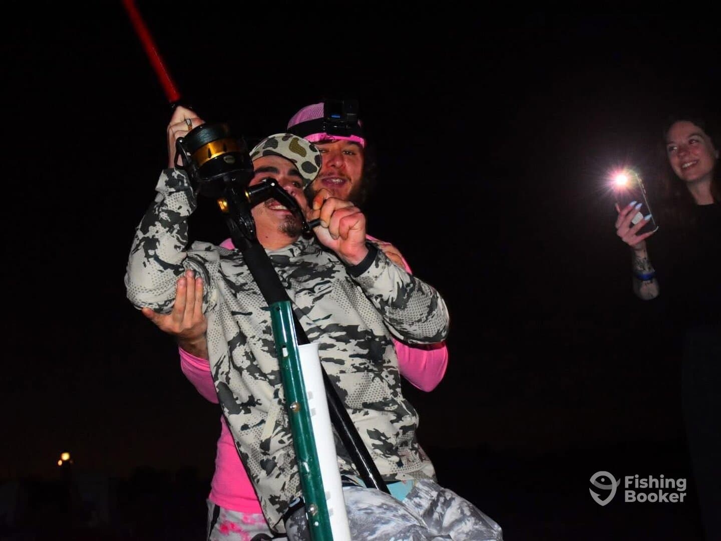 Two anglers enjoying a night fishing experience, with one preparing to cast while the other captures the moment on camera.