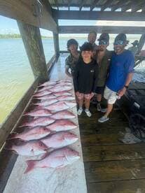 A group of anglers proudly displaying their catch of Red Snapper on a dock after a successful fishing trip.