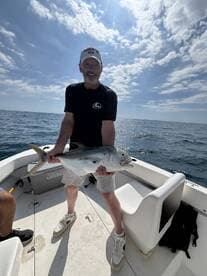 Angler proudly displaying a large fish on a sunny day aboard a fishing boat.