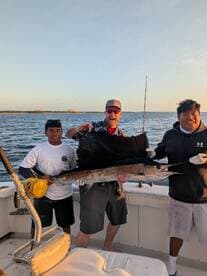 A group of anglers proudly displaying a large Sailfish on a boat during a fishing trip.