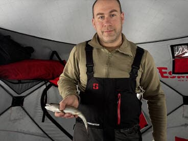 Angler proudly displaying a freshly caught fish inside an ice fishing shelter, showcasing the winter fishing experience.