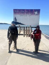 Two anglers proudly display their catch of Redfish in front of a 'Catch Of The Day' sign at a dock in Rockport, Texas.