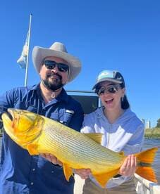 Two anglers proudly displaying a large Golden Dorado caught during a sunny fishing trip.