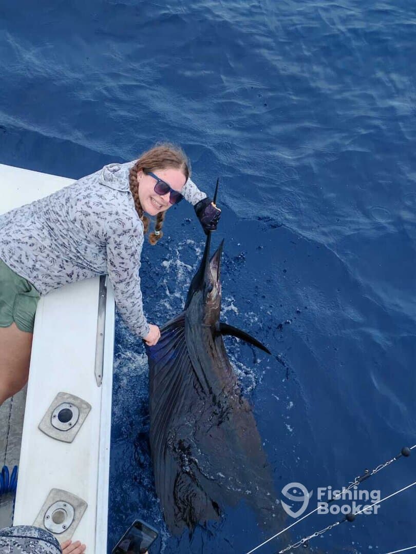 A young angler joyfully holding a large Sailfish while fishing offshore, showcasing a successful catch.