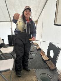 Angler proudly displaying a Crappie caught while ice fishing in a tent setup.