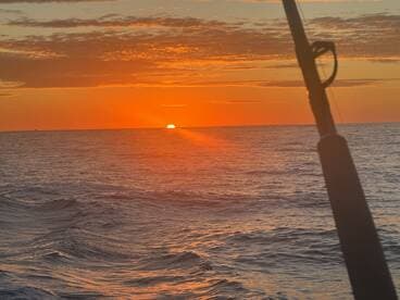 A stunning sunset over the ocean, captured from a fishing boat, showcasing the tranquil beauty of a fishing trip.