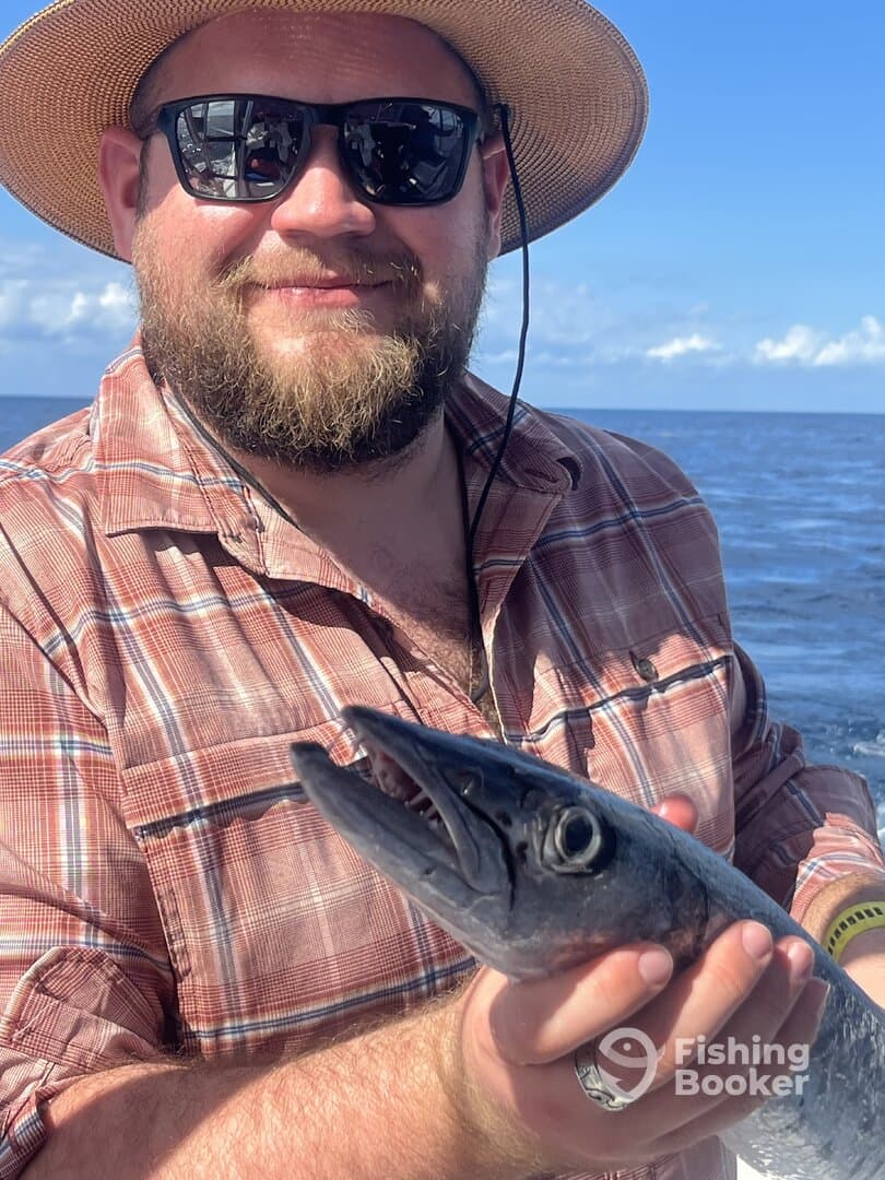Angler proudly displaying a large Barracuda while fishing offshore, showcasing a sunny day on the water.