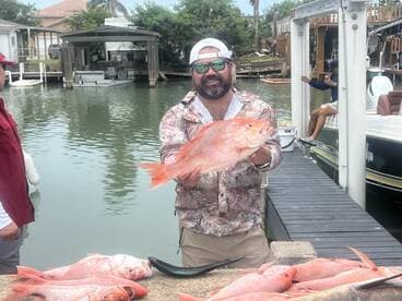 Angler proudly displaying a large Red Snapper at the dock, surrounded by a successful catch after a day of fishing.