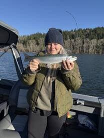 A proud angler holding a Rainbow Trout while fishing on a scenic lake surrounded by lush greenery.