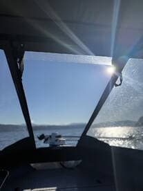 View from inside the boat showcasing the helm area with sunlight streaming through the windows, set against a backdrop of calm waters and distant mountains.