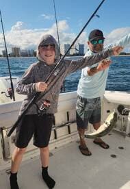 A young angler proudly displaying a fish while fishing with an adult companion on a boat, enjoying a day on the water.