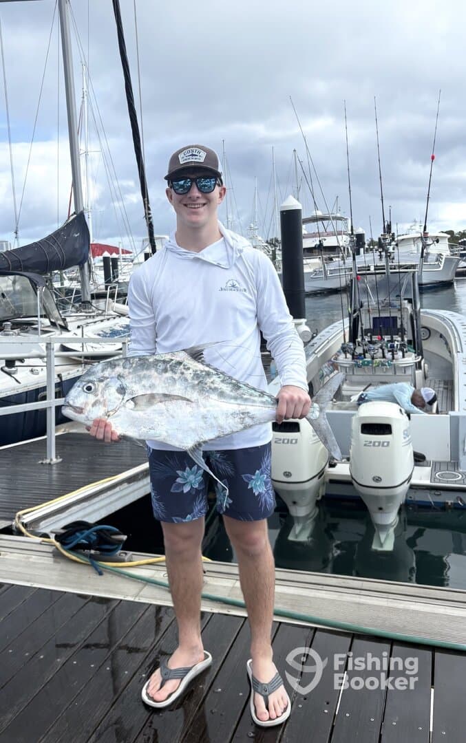 Young angler proudly holding a large fish at the marina after a successful fishing trip.