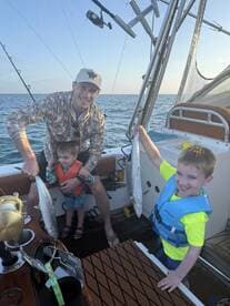A family fishing trip on a boat with two young boys proudly displaying their catches of Spanish Mackerel, enjoying a beautiful sunset on the water.