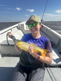 A smiling angler proudly displays a vibrant yellow fish while fishing on a small boat, showcasing a sunny day on the water.