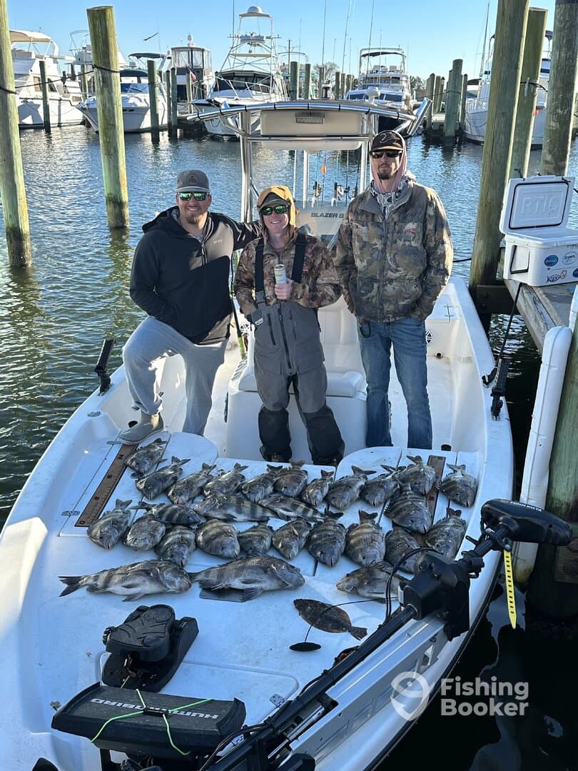 Three anglers proudly displaying their catch of multiple Black Drum and Flounder on the boat after a successful fishing trip.