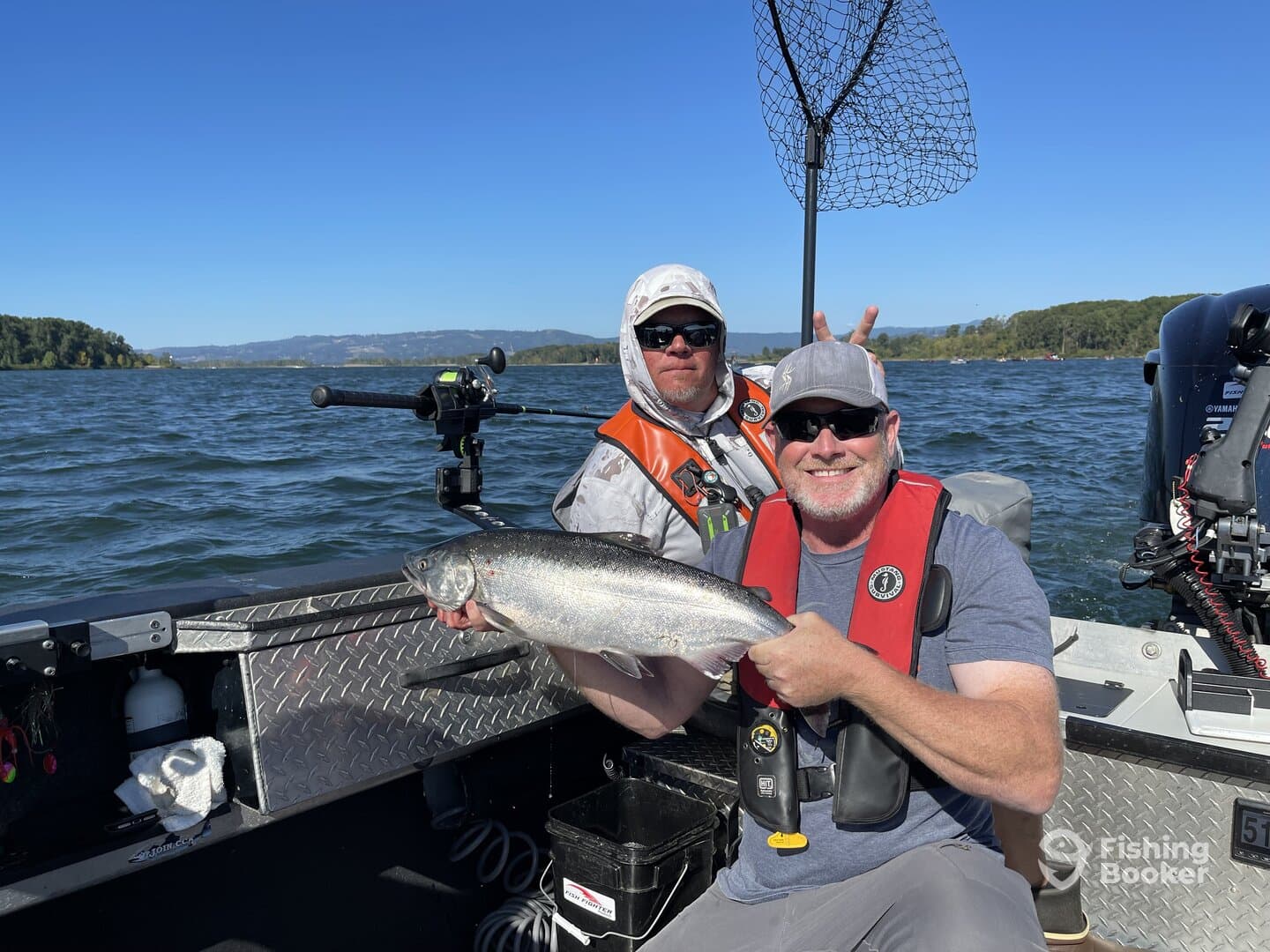 Two anglers proudly displaying a large Salmon while fishing on a scenic river, showcasing a fun day on the water.
