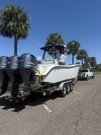 A sleek center console boat equipped with triple Yamaha outboards, parked under palm trees on a sunny day, ready for a fishing adventure.