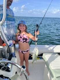 A young angler proudly holding a Yellowtail Snapper while fishing on a boat, showcasing a fun family fishing experience.