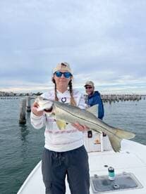 Angler proudly displaying a large Snook while fishing from a boat, with a scenic backdrop of pilings and waterfront buildings.