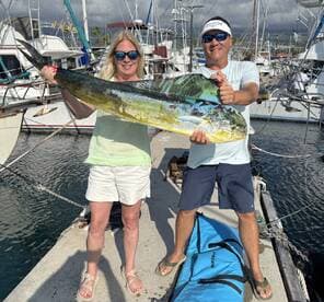 Two anglers proudly displaying a large Mahi Mahi at the dock, showcasing their successful fishing trip.