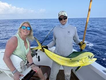 A woman and a fishing guide proudly display a vibrant Mahi-Mahi while on a fishing charter in open waters.