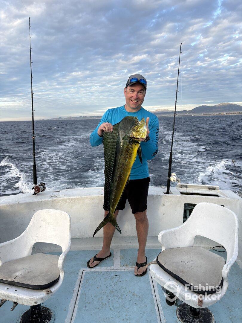 Angler proudly displaying a large Mahi Mahi aboard a fishing boat, with a scenic ocean backdrop.