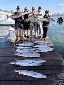 A group of anglers proudly displaying their catch of Barracuda on the dock after a successful fishing trip.