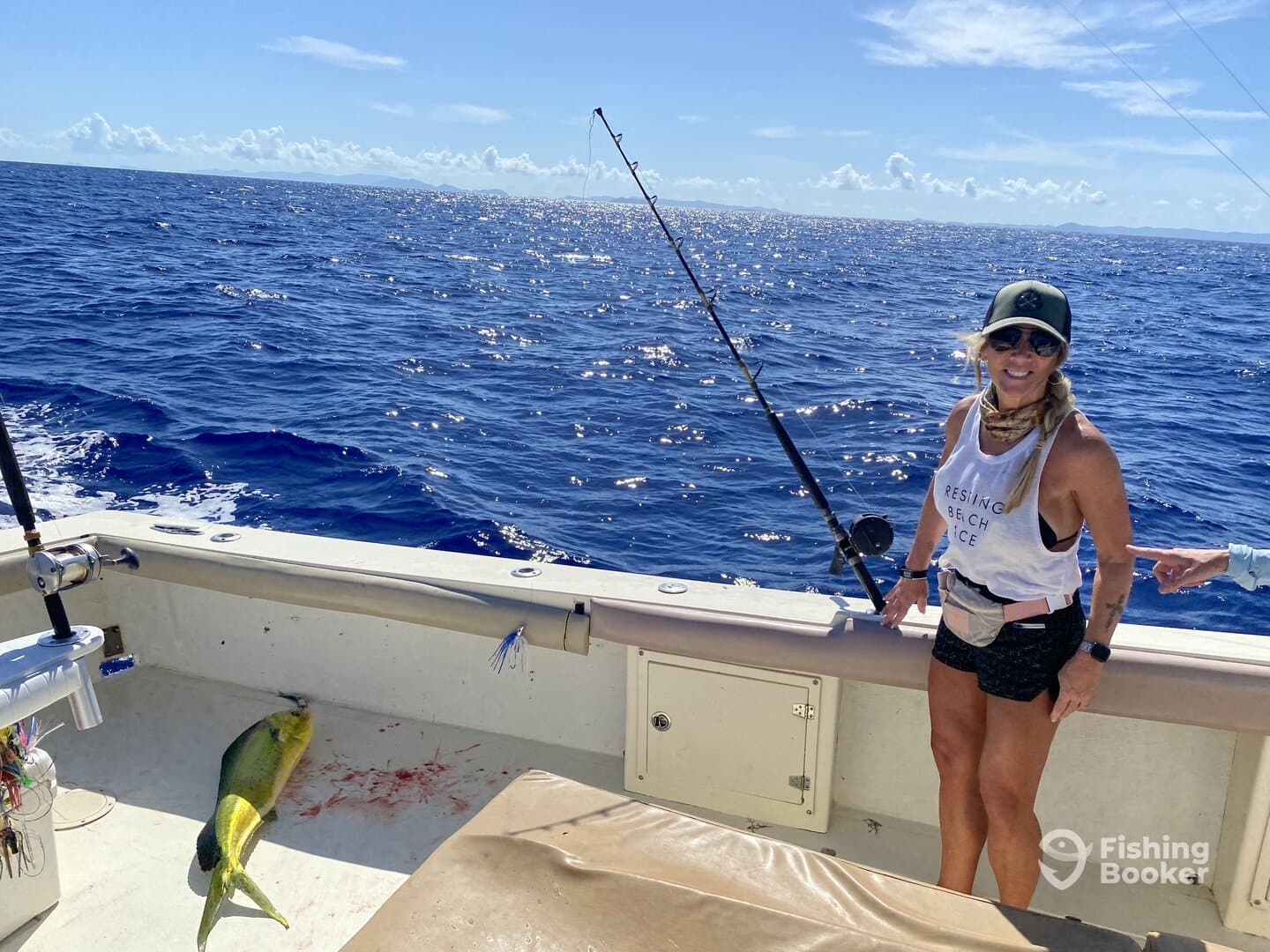 A female angler stands on a boat with a vibrant Mahi Mahi on the deck, enjoying a sunny day of deep-sea fishing.