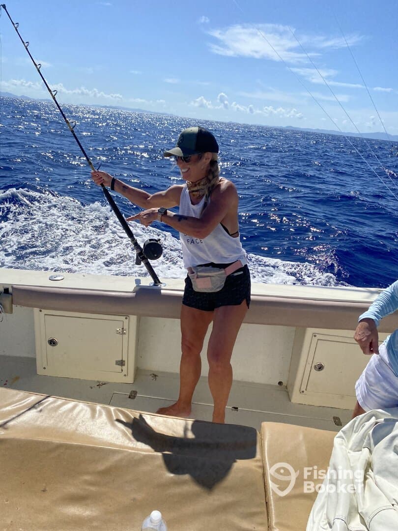 A female angler actively reeling in a fish while enjoying a sunny day on a fishing boat in open waters.