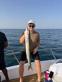A young angler proudly displaying a large Barracuda while fishing on a boat in open waters.