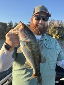 Angler proudly displaying a large Largemouth Bass while fishing on a serene lake.