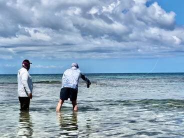 Two anglers casting lines while wading in shallow waters, enjoying a day of fishing under a partly cloudy sky.