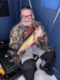 An angler proudly displaying a large Walleye while ice fishing in a cozy shelter.