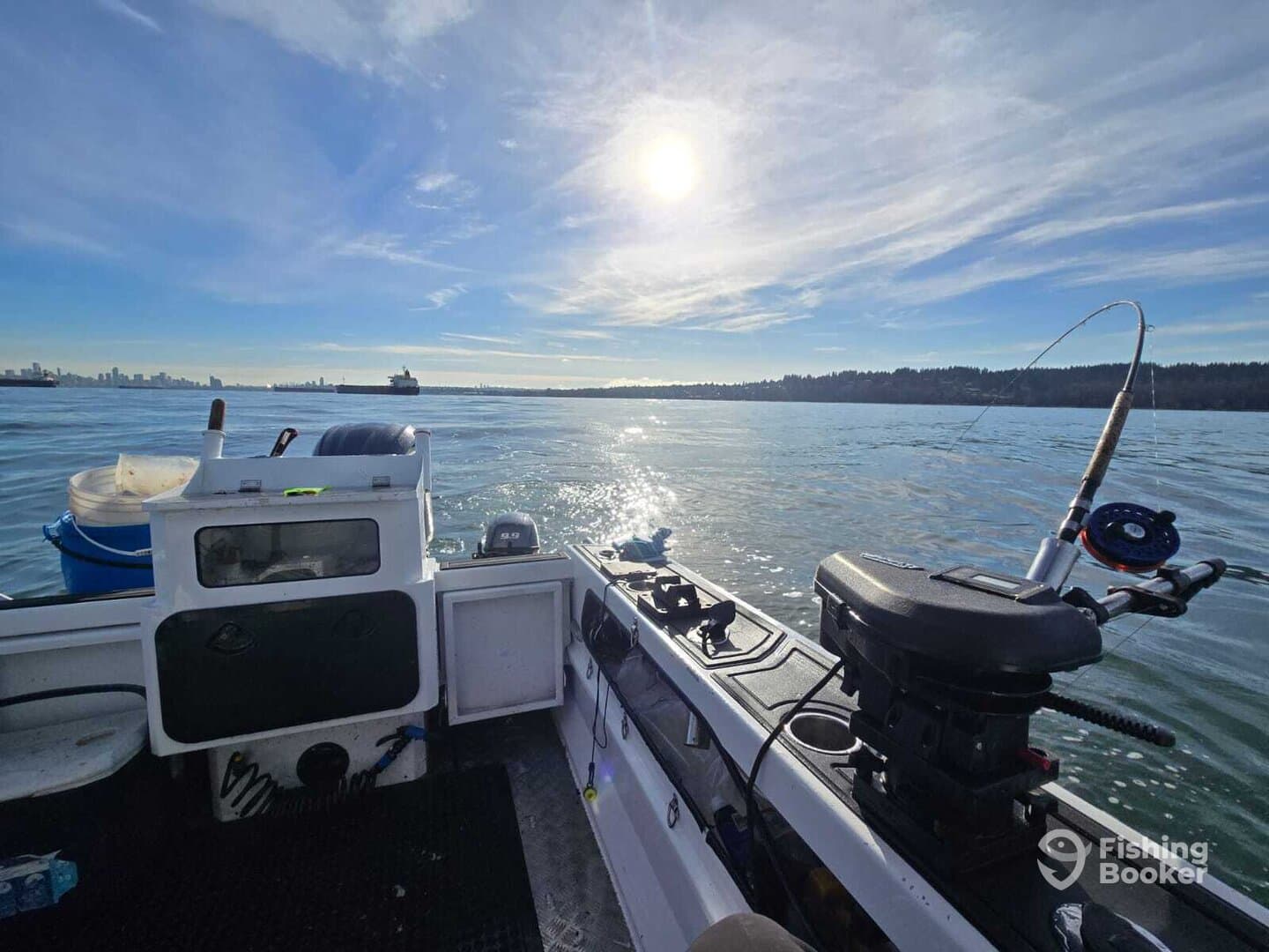 Interior view of a fishing boat with a scenic backdrop of the water and skyline, showcasing the helm and fishing gear.