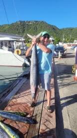 An excited angler proudly displaying a large fish at the dock, surrounded by a scenic backdrop of hills and boats.