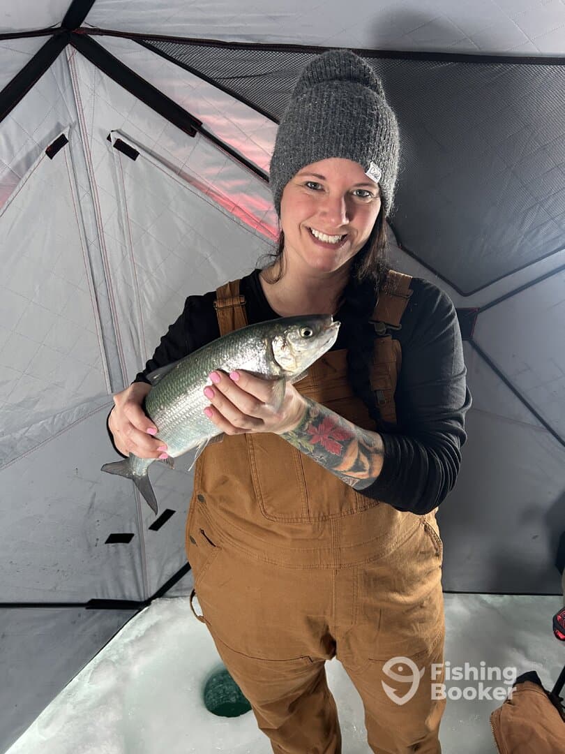A proud angler holding a freshly caught fish inside an ice fishing shelter, showcasing the excitement of winter fishing.