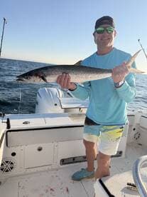 Angler proudly displaying a large King Mackerel while fishing on a boat in open waters.